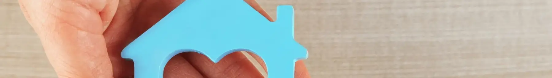 open hand holding wooden flat shape of house with heart shape cut out