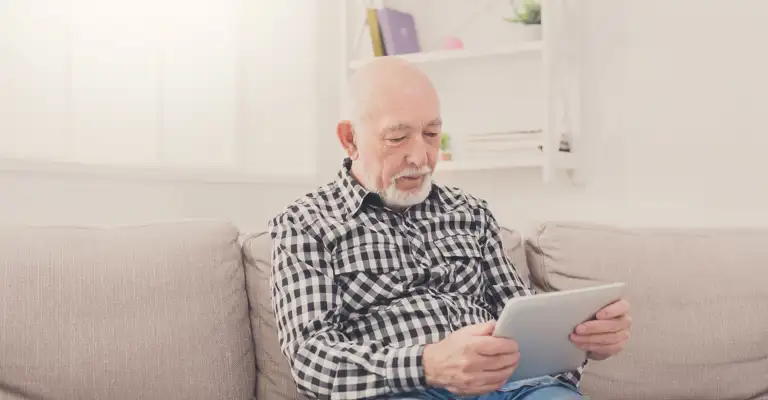Older Man On Tablet Sitting On Sofa Web